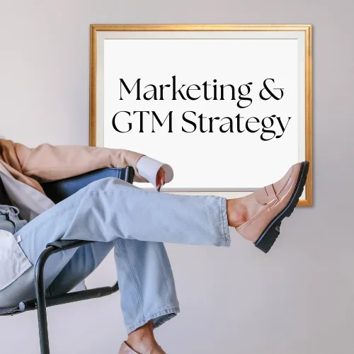 Person relaxing in chair with crossed legs, wearing casual attire and stylish shoes, next to a framed sign displaying "Marketing & GTM Strategy," emphasizing Sanguine's focus on strategic business growth and marketing expertise.