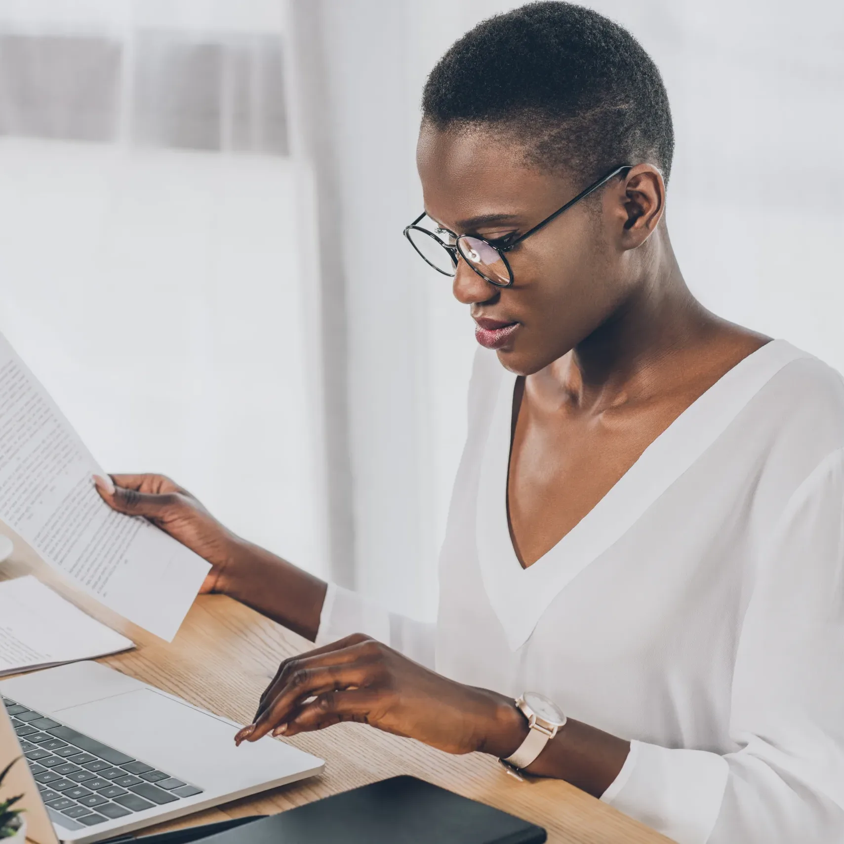 stylish attractive african american businesswoman holding contract and using laptop in office
